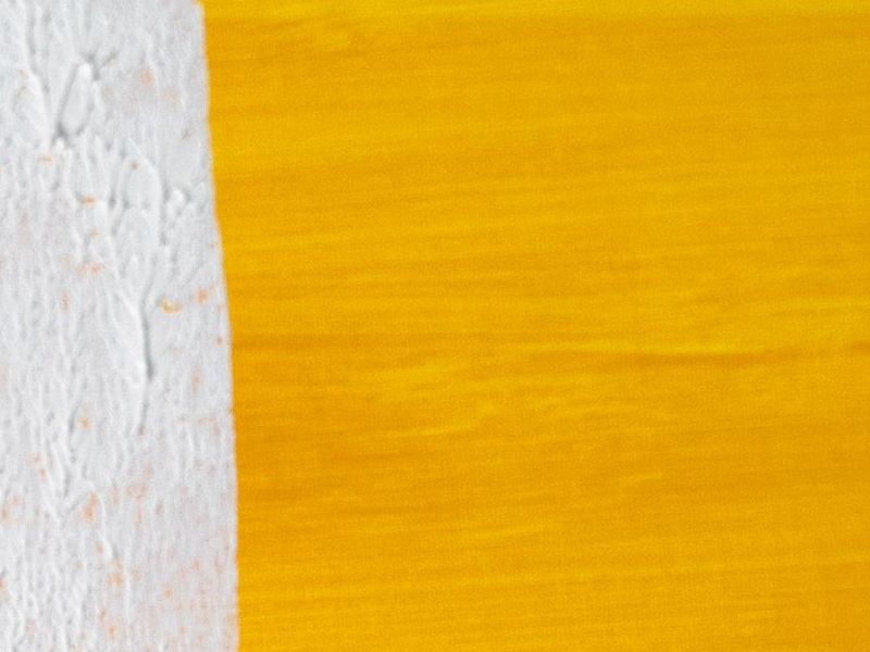 Close-up of a fresh white paint edge on a yellow surface (representative stock photo)