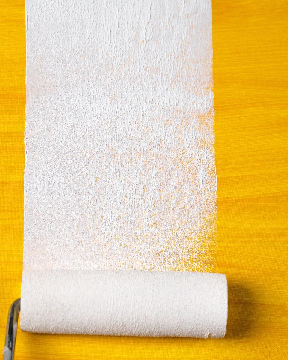 A paint roller laying a fresh white coat over a yellow surface (representative stock photo)